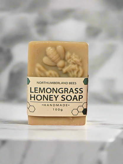 A bar of Honey Lemongrass Soap with a label stating 'Northumbrian Bees Lemongrass Honey Soap - Handmade 100g' against a marble background.