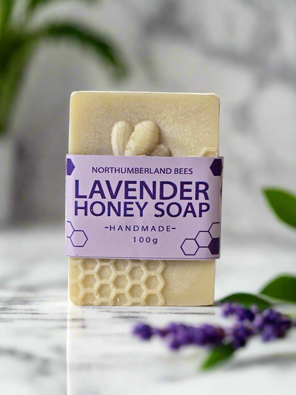Lavender honey soap bar with a purple label on a marble surface with blurred greenery in the background
