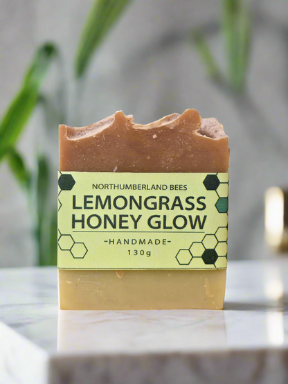 A bar of Lemongrass Honey Glow soap with a yellowish hue and a label that reads 'Northumberland Bees' and 'Lemongrass Honey Glow - handmade' with a weight indication of '130g'.